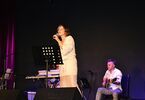 Zdjęcie: kobieta z mikrofonem na scenie, w tle muzycy