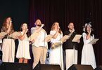 Zdjęcie: grupa osób w jasnych strojach śpiewających na scenie