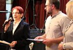 Seniorka trzymająca mikrofon, obok niej mężczyzna i kobieta