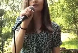 Pola Deptuła śpiewa do mikrofonu na tle drzew