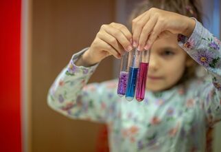 Dziewczynka trzymająca trzy fiolki z płynem o różnych kolorach.