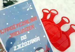 Zdjęcie kartki z informacją o wypożyczalni jabłuszek do zjeżdżania. Obok na śniegu leżą cztery czerwone jabłuszka.