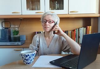 Marzena Szychułda siedzi przy stoliku z laptopem i filiżanką herbaty i rozmawia przez telefon.