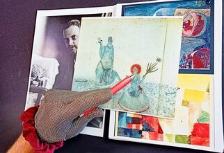 Ręka odziana w srebrną rękawiczkę wskazuje czerwonym długopisem na jedną z prac Paula Klee