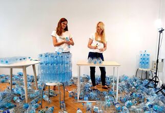 Dwie kobiety tworzą fotel z plastikowych butelek. Wokół porozrzucane plastikowe butelki