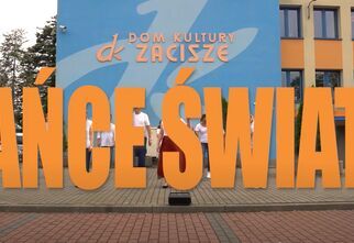 Napis Tańce Świata na tle budynku DK Zacisze i grupy tancerzy
