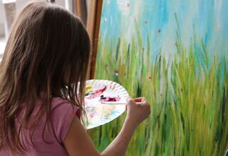 Dziewczynka maluje akwarelami obraz przedstawiający łąkę