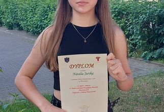 Natalia trzyma dyplom za zajęcie I miejsca w konkursie wokalnym na tle zieleni