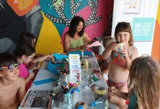 Dzieci zgromadzone wokół stoiska Domu Kultury Zacisze, na którym znajdują się między innymi flamastry i inne materiały do malowania