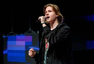 Młody mężczyzna śpiewa na scenie, w lewej ręce trzyma mikrofon