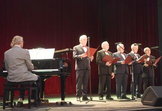 Pięciu mężczyzn w garniturach scenie i akompaniator na scenie. Foto: Dom Kultury Miś