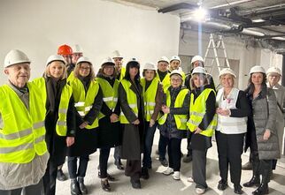 Zdjęcie: grupa ludzi w żółtych odblaskowych kamizelkach i kasakach na terenie budowy