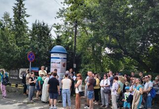 Zdjęcie: grupa ludzi stojąca przy okrągłym słupie ogłoszeniowym Domu Kultury Zacisze