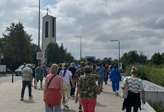 Zdjęcie: spacerująca grupa ludzi, w tle wieża kościoła z krzyżem