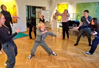 Zdjęcie: grupa osób w choreografii na parkiecie, w tle kolorowe obrazy