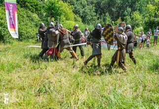 Zdjęcie: odwzorowująca walkę grupa w strojach rycerskich z mieczami i tarczami, źródło: Urząd Dzielnicy Targówek