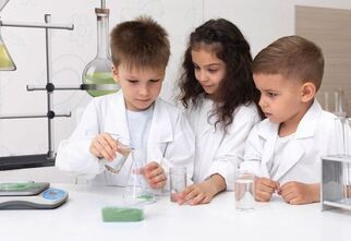 Zdjęcie: troje dzieci w białych fartuchach przy probówkach i szklanych naczyniach