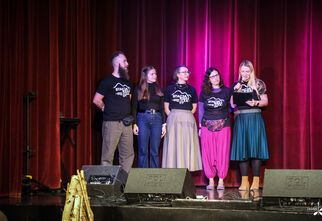 Zdjęcie: Cztery kobiety i mężczyzna na scenie, kobieta w długich blond włosach z mikrofonem w ręku