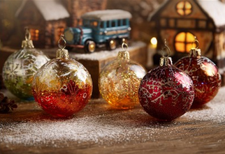 Zdjęcie: Kolorowe bombki na drewnianym podłożu lekko oprószonym śniegiem, z tyłu dwa domki lampiony i auto w starym stylu przypominające bombkę - zawieszkę na choinkę