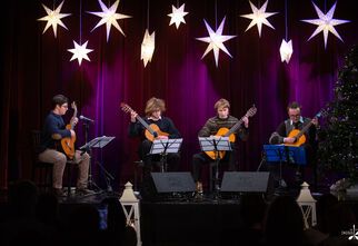 Zdjęcie: Czworo młodych mężczyzn siedzących na krzesłach z gitarami na scenie, nad nimi wiszące ozdobne białe gwiazdy