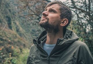 Zdjęcie: mężczyzna w średnim wieku, z brodą, zapatrzony w górę, w tle drzewa