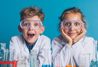 Zdjęcie: dwójka nastolatków chłopiec i dziewczyna w okularach ochronnych w białych fartuchach przy stole z probówkami i szklanymi naczyniami na niebieskim tle