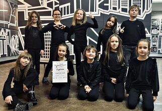 Zdjęcie: Uśmiechnięte dzieci w czarnych strojach, jedna dziewczynka trzyma dyplom