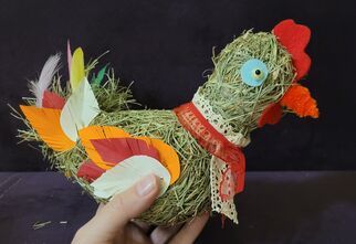 Zdjęcie: kura ze słomy ozdobiona kolorowymi elementami z materiału, widoczna ręka trzymająca całość