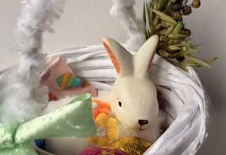 Zdjęcie: biały koszyczek z włóczki ozdobiony kokardą i suszonymi roślinami, w środku zajączek i pisanka