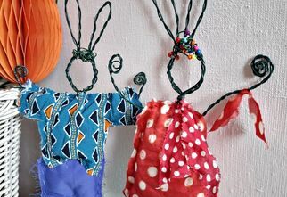 Zdjęcie: dwa zające wykonane ręcznie, z drutu i kolorowych ubranek, oparte o ścianę, fragment kosza wiklinowego