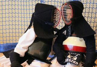 Zdjęcie: dwóch młodych zawodników siedzących na podłodze w tradycyjnych strojach Kendo z mieczami