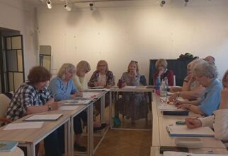 Zdjęcie seniorek i seniorów rozwiązujacych zadania na stole