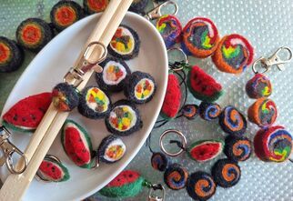 Zdjęcie: kolorowe breloczki z filcu przypominające sushi i arbuzy rozłożone w białej formie i wokół niego na jasnym tle