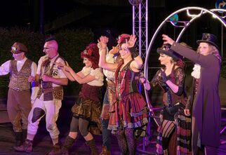 Zdjęcie: grupa osób w steampunkowych kostiumach na scenie, fioletowe oświetlenie, obok metalowa konstrukcja z zegarem,