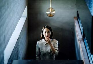 Zdjęcie: kobieta stojąca na schodach w kraciastej marynarce lekko zasłaniająca twarz ręką, fot. Filmweb
