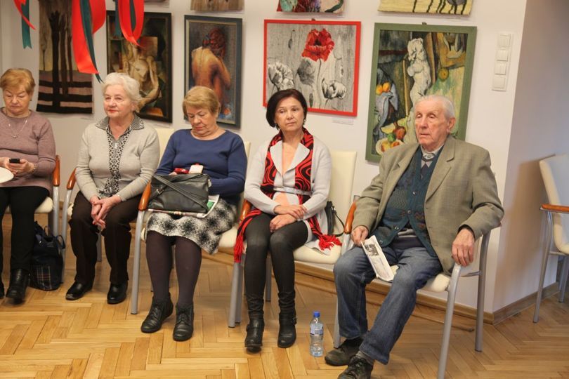 Seniorki i senior siedzący na krzesłach w pomieszczeniu z kolorowymi obrazami