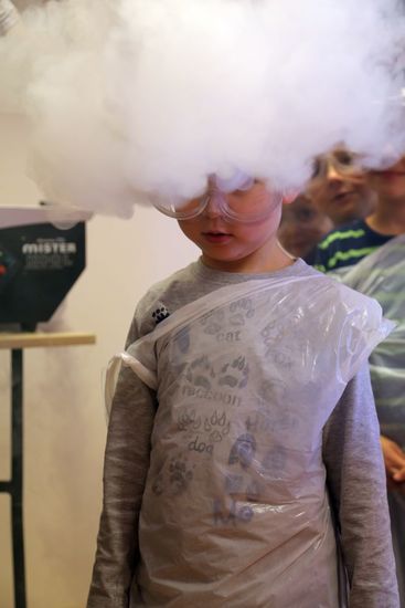 Chłopczyk ubrany w ochronną folię i gogle ochronne schowany za chmurą dymu