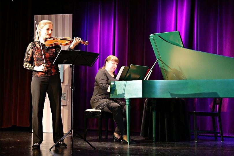 Kobieta gra na skrzypcach, za nią kobieta gra na fortepianie