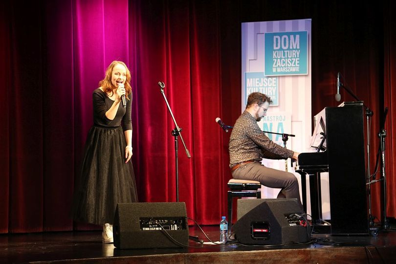 Dziewczyna śpiewa, a obok niej mężczyzna gra na pianinie
