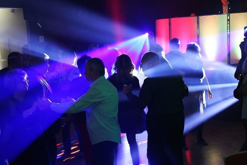 Grupa ludzi tańczy na sali. Tłum oświtlony kolorowymi światłami.