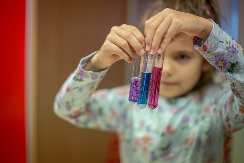 Dziewczynka trzymająca trzy fiolki z płynem o różnych kolorach.
