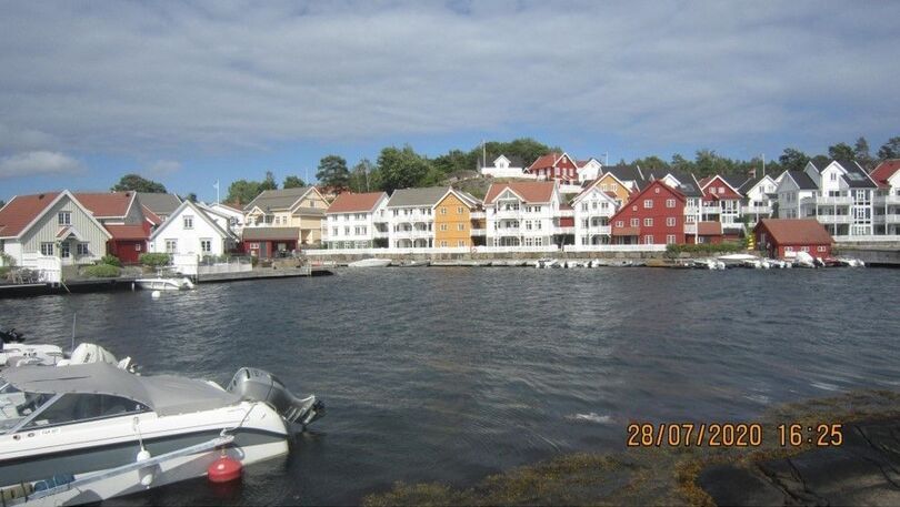 Zdjęcie z aparatu przedstawiające skandynawską zatokę z motorówką i rzędem domów na linii brzegowej.