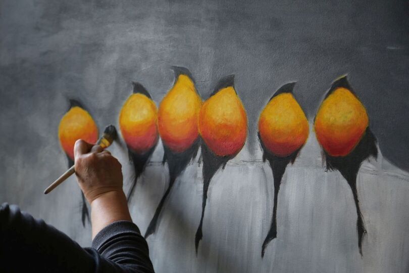 Uczestnik maluje ptaszki z żółto-pomarańczowymi brzuszkami na szarym tle