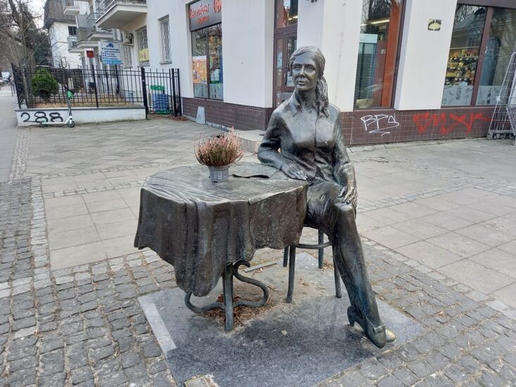 Pomnik: kobieta w średnim wieku siedzi przy okrągłym stole.
