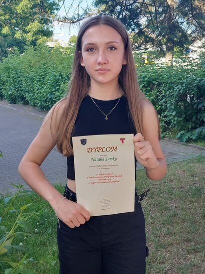 Natalia trzyma dyplom za zajęcie I miejsca w konkursie wokalnym na tle zieleni