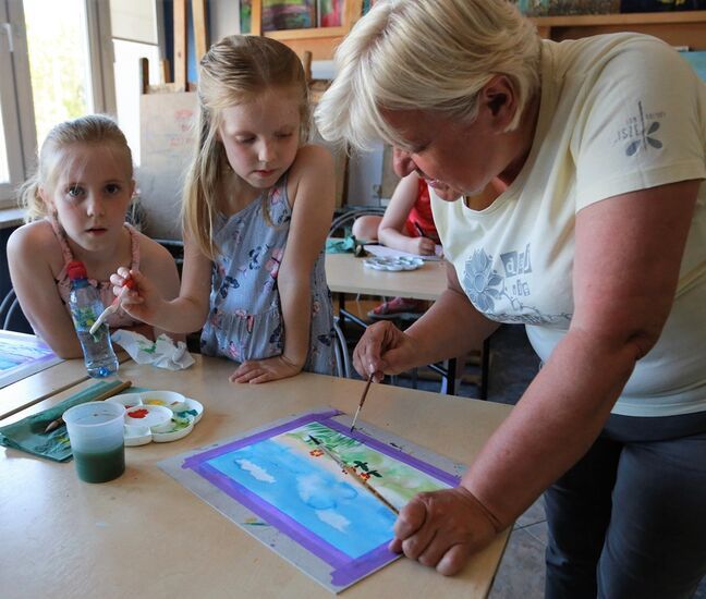 Instruktorka tłumaczy dzieciom technikę malowania i kompozycję