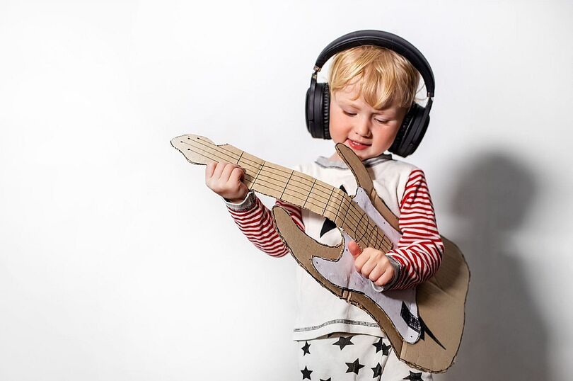 Dziecko ze słuchawkami na uszach grające na gitarze wyciętej z tektury