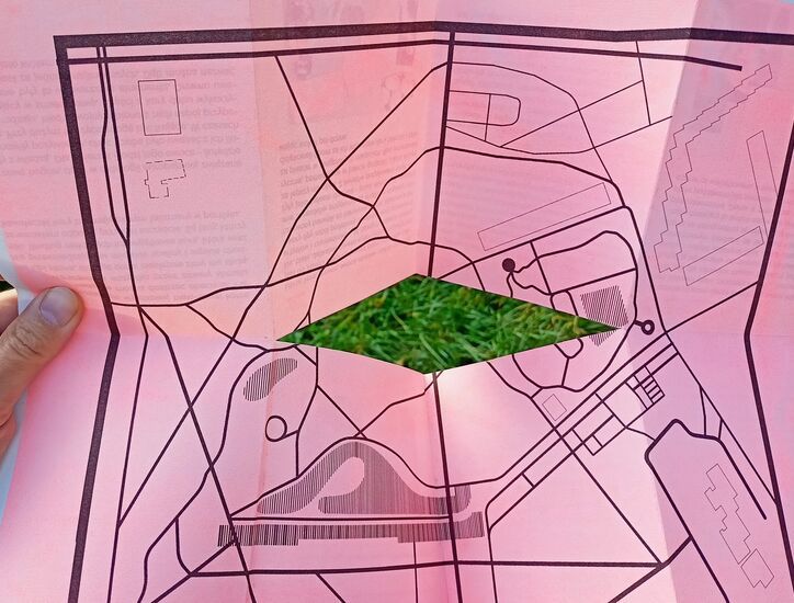 Mapa z konturami Parku Rzeźby na różowym tle z otworem w środku w kształcie rombu z widokiem na trawę