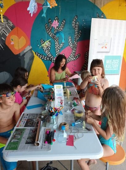 Dzieci zgromadzone wokół stoiska Domu Kultury Zacisze, na którym znajdują się między innymi flamastry i inne materiały do malowania