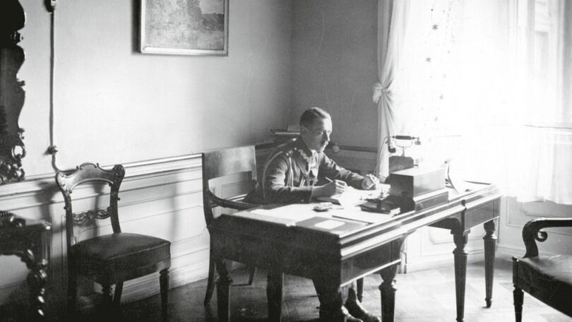 Stare zdjęcie przedstawia siedzącego za biurkiem mężczyznę w mundurze
